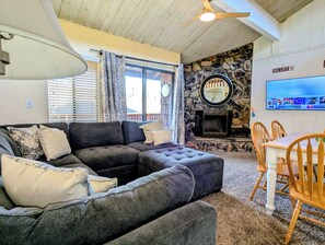 A living room with a sectional sofa, a fireplace, a TV, and a dining area with wooden chairs.