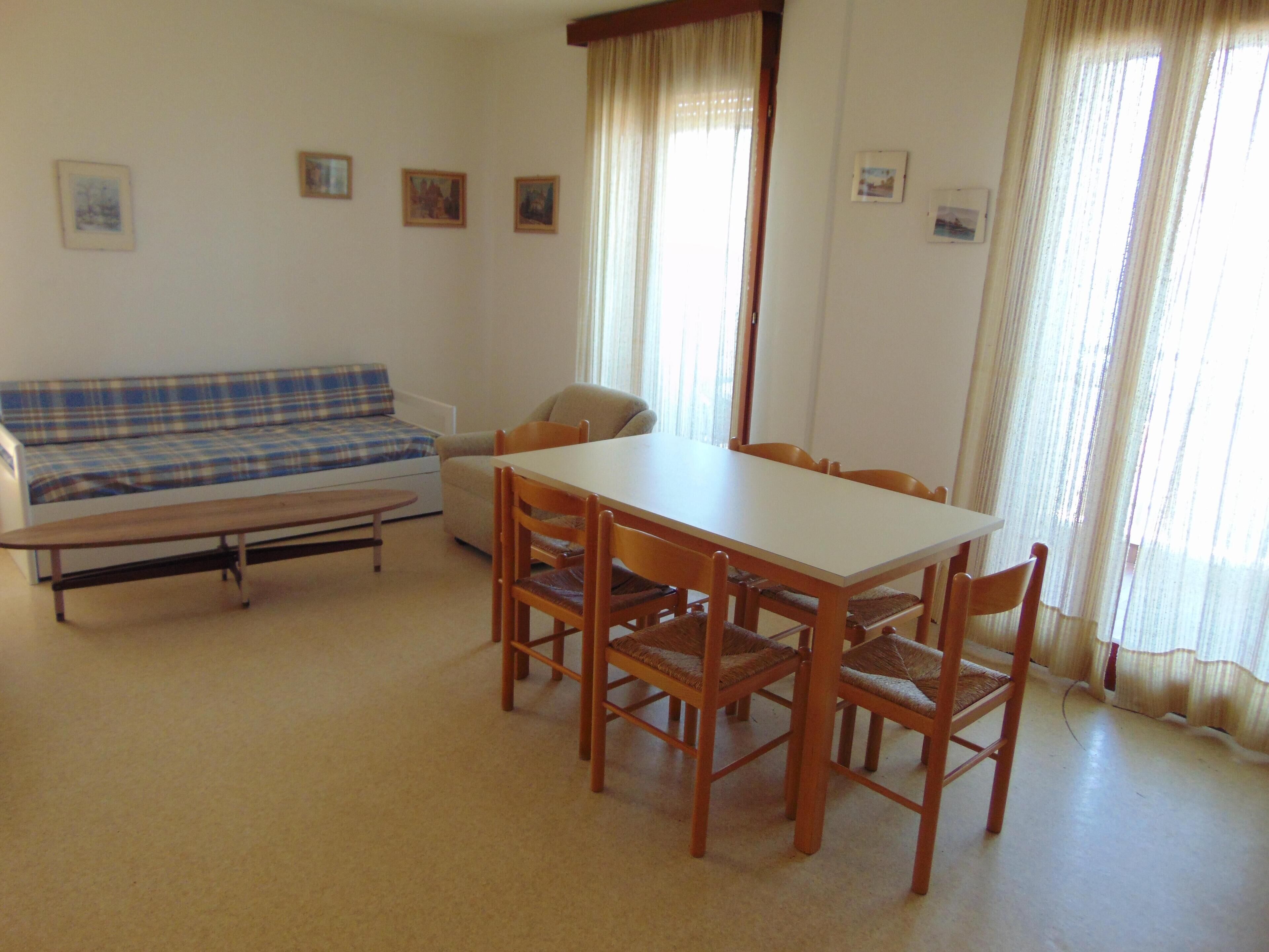 Ein Wohnzimmer mit Sofa, Esstisch und Stühlen sowie einem Fenster mit Vorhängen.