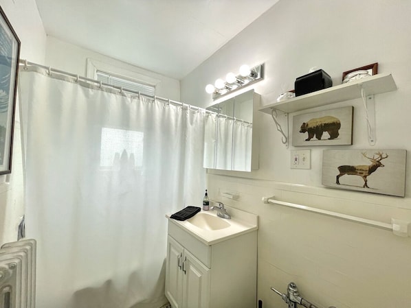 Ein Badezimmer mit einem weißen Waschbecken, einem Spiegel und einer Duschvorhang. Über dem Spiegel hängen zwei gerahmte Bilder an der Wand.
