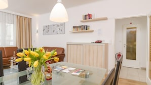 A modern living room with a glass coffee table, a brown leather sofa, a vase of yellow tulips, and a bookshelf with books and a framed picture.