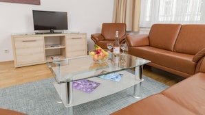 A modern living room with a glass coffee table, leather sofa, and a wooden cabinet with a flat-screen TV.
