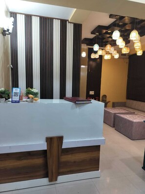 A reception desk with a modern design, a seating area with sofas, and hanging pendant lights. - Hotel Vista (Noida)