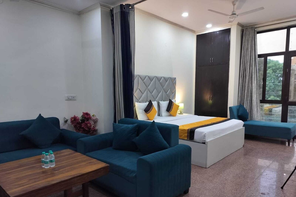 A hotel room with a bed, two sofas, a small table, and a window with curtains.