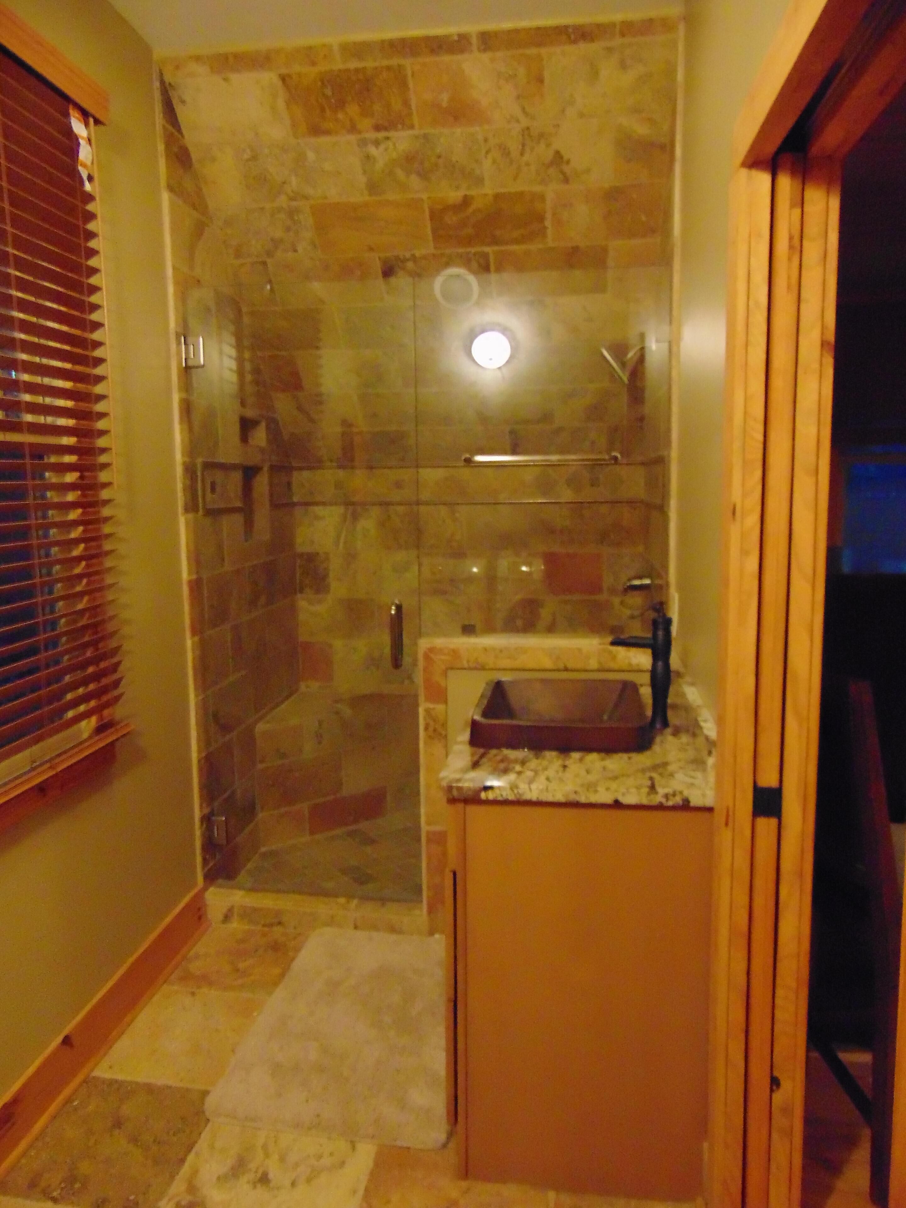 Une petite salle de bain avec une douche à parois de verre, un lavabo avec un plan de travail et une porte en bois.