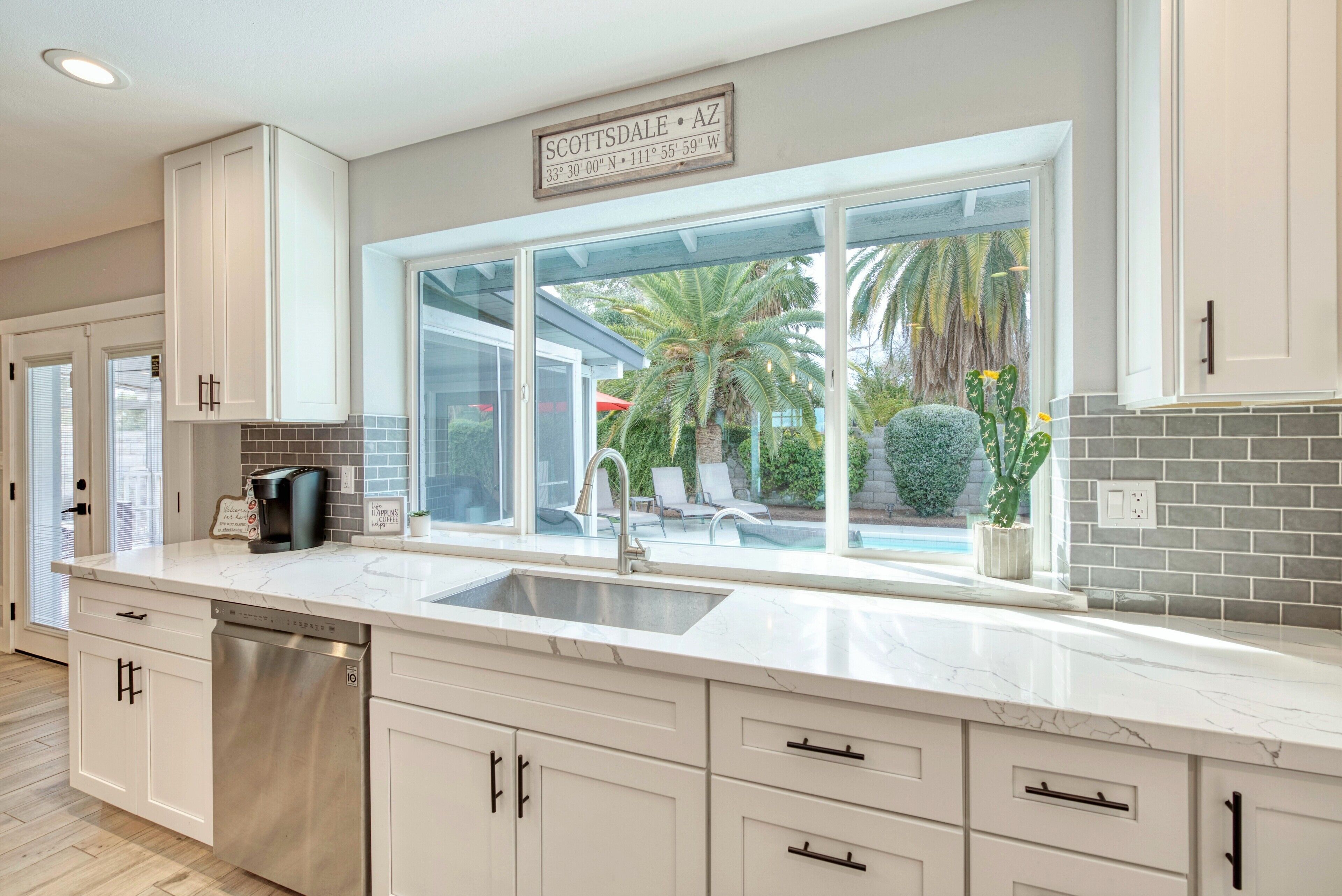 A modern kitchen with a large window, white cabinetry, and a built-in dishwasher.
