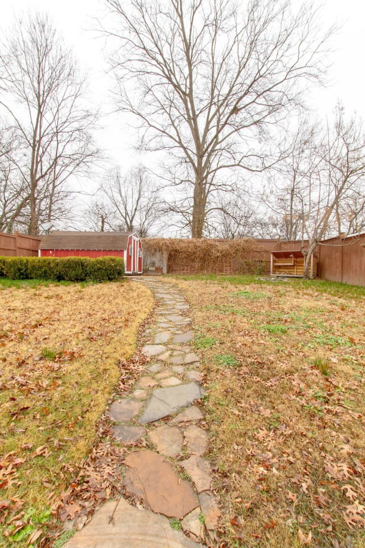 A stone pathway leading to a red and white shed in a grassy yard with leaf-covered ground.