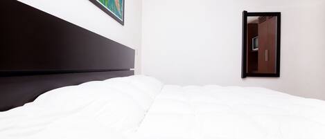 Une chambre d’hôtel avec un grand lit, une tête de lit, un climatiseur fixé au mur, un tableau encadré et une porte dotée d’un miroir.
