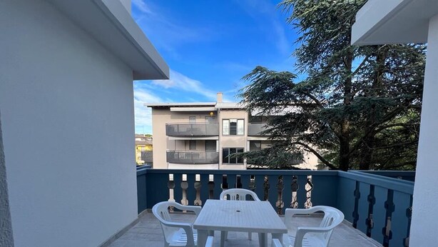 Un balcon avec une table et des chaises, une rambarde bleue et un bâtiment en arrière-plan.