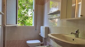Une salle de bain comprenant des toilettes, un bidet, un lavabo et une fenêtre donnant sur un espace verdoyant.