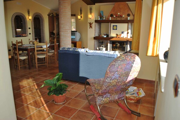 Una sala de estar acogedora con un sofá, un sillón estampado, un comedor con sillas y una mesa, y una chimenea.
