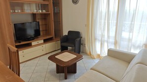 A living room with a TV, wooden entertainment unit, a sofa, and a chair.