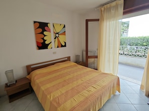 A bedroom with a bed, a nightstand, a window with curtains, and a balcony with a railing.