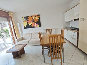 A modern kitchen with white cabinets, a dining table with chairs, a sofa, and a large floral artwork on the wall.