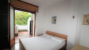Une chambre à coucher comprenant un lit, une table de chevet, une commode, une porte donnant sur un balcon et une petite table.