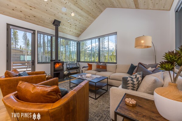 A modern living room with leather sofas, a wooden coffee table, and a large window with a mountain view.