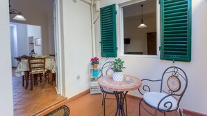 Un comedor con una mesa redonda y sillas, una planta en maceta y una ventana con contraventanas verdes.