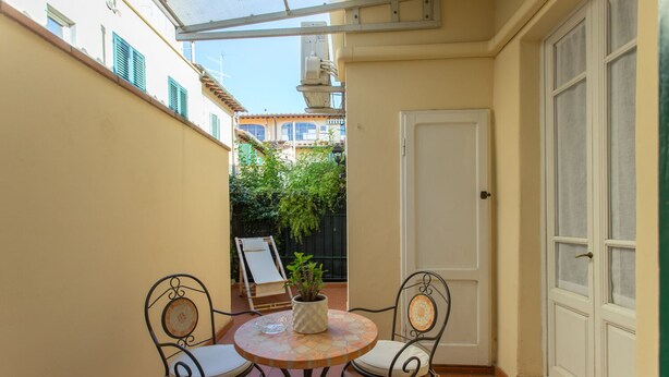 Un pequeño patio con una mesa redonda y dos sillas, una planta en maceta y una puerta.