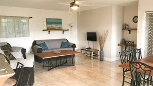 A living room with a sofa, coffee table, TV, and dining area with chairs and a table. - YD Rooftop Lounge ocean view salt water pool with mountain view large 2bdrm  (Montego Bay)