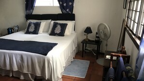 A bedroom with a bed, a nightstand, a fan, and a window with curtains. - ECO FRIENDLY QUAINT PALMETTO Studio (Bridgetown)