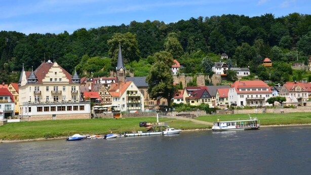 A riverside town with historic buildings, a church, and boats docked along the water.