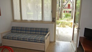 A room with a blue plaid sofa, a wooden desk with a television, and a window with curtains. - Villa Chiara 2 - Lignano (Lignano Sabbiadoro)