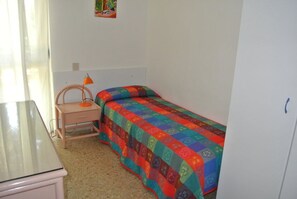 A small, simple room with a bed, a desk, and a chair.