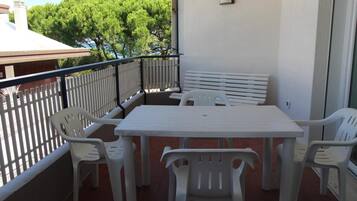 Ein Balkon mit weißem Tisch und Stühlen, einer weißen Bank und einem weißen Geländer.