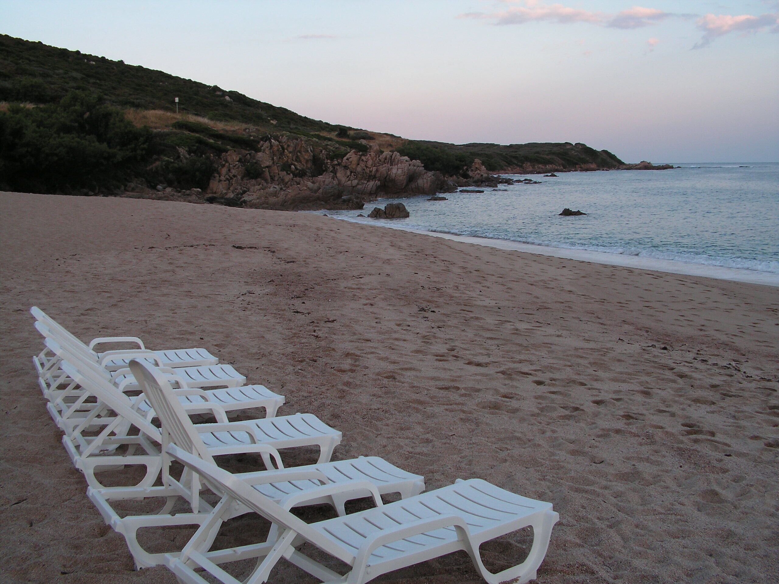 Une plage où l’on trouve des chaises longues en plastique blanc, alignées face à l’océan.