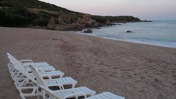 Une plage où l’on trouve des chaises longues en plastique blanc, alignées face à l’océan.