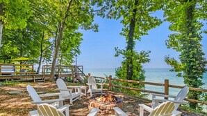 A deck with Adirondack chairs, a fire pit, and a view of the lake.