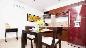 A modern kitchen with a dark wooden dining table, white cushioned chairs, a red refrigerator, and a microwave above the counter. - Kingsize 1bdr apt w/private balcony&jacuzzi, common rooftop w/pool (unit104) (Playa del Carmen)