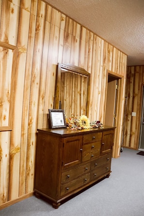 A wooden-paneled room with a large wooden dresser against the wall, a framed certificate on top, and a mirror above the dresser. - Get Away from the Bustle of the City (Lockridge)