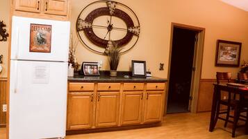 A kitchen with wooden cabinets, a refrigerator, a wall clock, and a dining area with chairs.