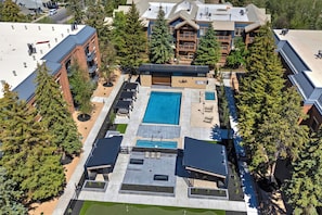 An aerial view of a hotel with a central swimming pool, multiple balconies, and surrounding trees.