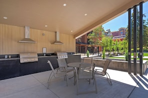 An outdoor patio with a grill, chairs, and a view of buildings.