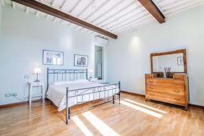 A bedroom with a metal bed frame, wooden dresser, and a ceiling with exposed beams.