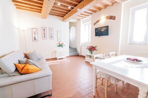 A spacious living area with a white sofa, a dining table, and a staircase leading to an upper floor.