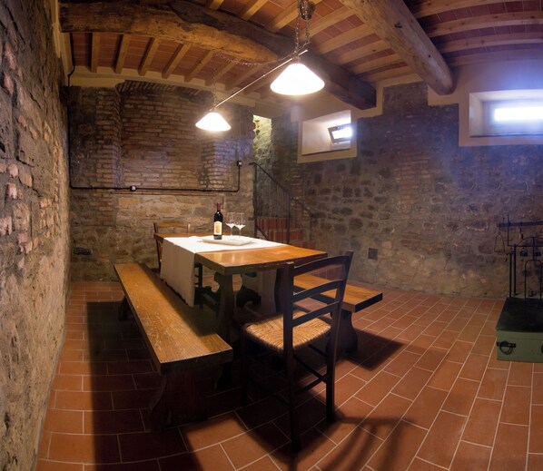 A rustic stone-walled room with a wooden table, benches, and a wine bottle. - Il Borgo degli Agrumi - L'Arancio (Uzzano)