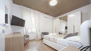 A modern hotel room with a flat-screen TV, a bed with a floral duvet, a wooden desk, and a large mirror. - Tow bedroom, perfect family size. Central location (free Wifi) (Roma)