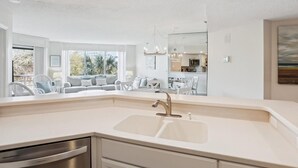 Una cocina moderna con un lavamanos doble, electrodomésticos de acero inoxidable y un comedor con mobiliario blanco.