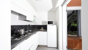 A modern kitchen with white cabinets, a black countertop, a stainless steel kettle, and a microwave.