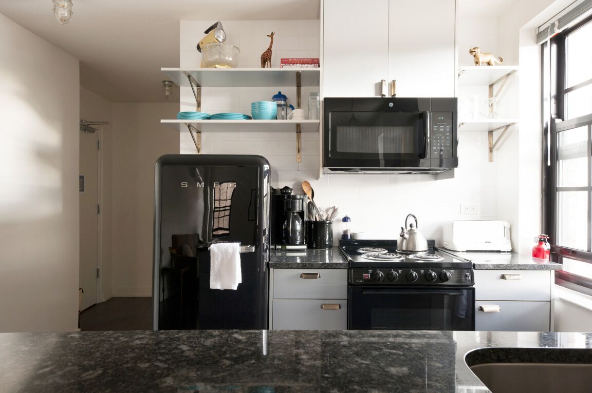 A modern kitchen with a black refrigerator, stove, and microwave. There are shelves above the stove with decorative items.