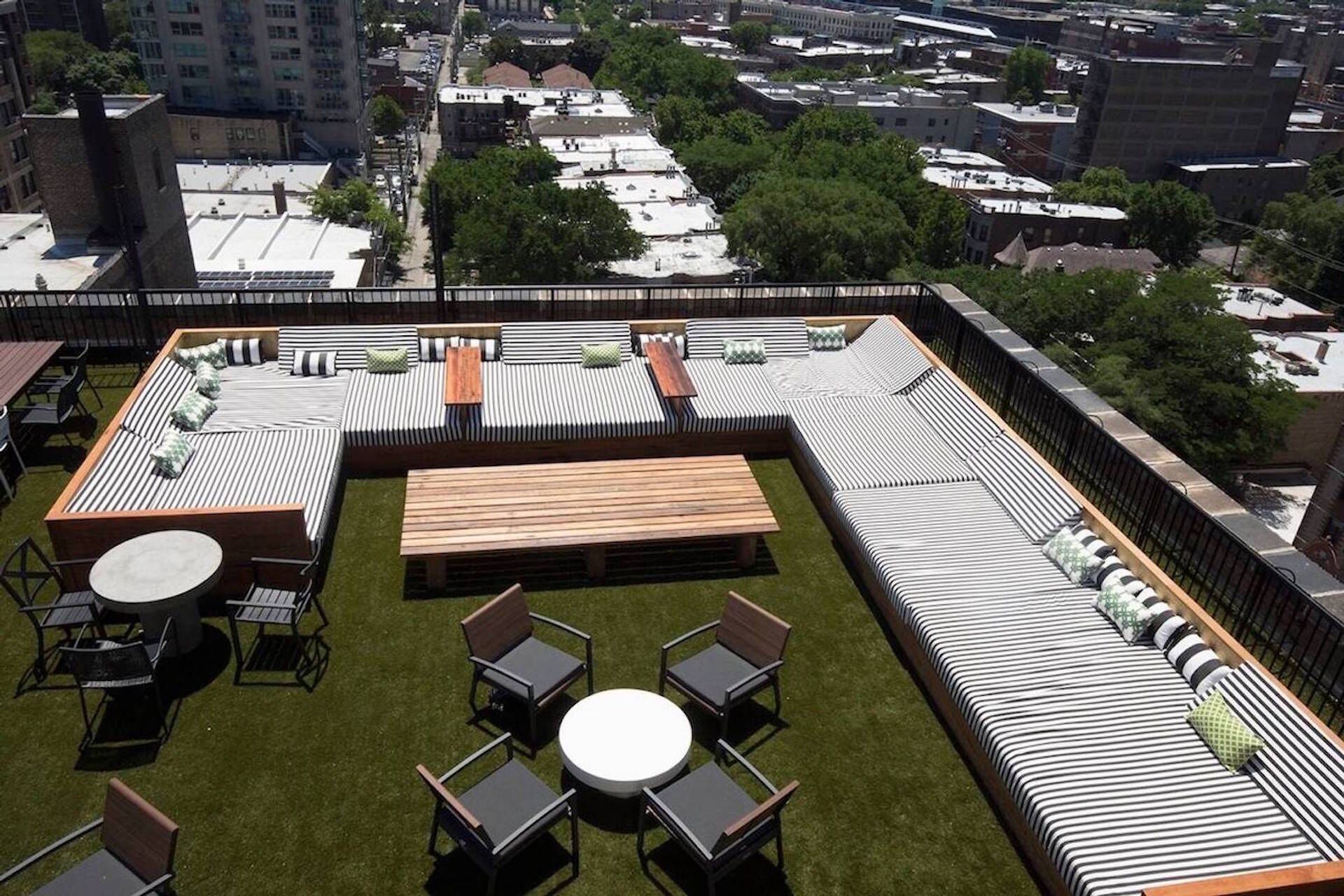 Una terraza en la azotea con un sofá largo y a rayas, una mesa de madera y una mesita redonda con sillas.