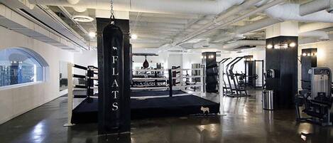 Une salle de sport équipée de rings de boxe, de machines de musculation et d’un sac de frappe sur lequel est écrit « FLATS ».