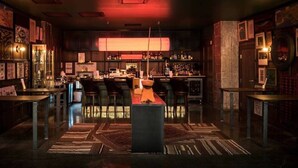 A bar area with a neon sign reading "LARRY'S," bar stools, a central bar counter, and a patterned rug on the floor.