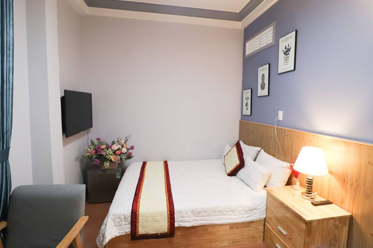 A neatly arranged bedroom with a bed, bedside table, lamp, and a wall-mounted TV.