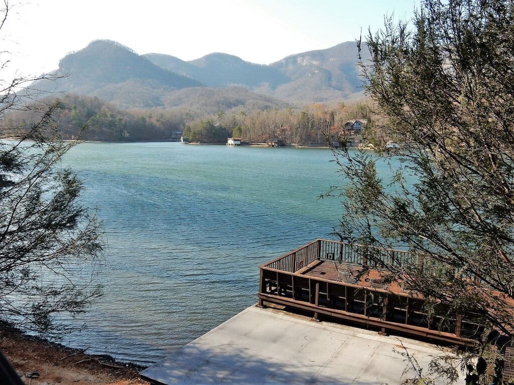 A lakeside view with a dock extending into the water, surrounded by trees and distant mountains.
