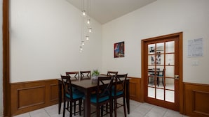 A dining area with a wooden table and chairs, a hanging light fixture, and a door leading to another room. - Vista Verde 102, Cozy Condo in Brownsville (Brownsville)