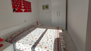A bedroom with a bed, a wardrobe, a nightstand, a red lamp, and a wall art piece. - Condominio Billa 8 - Lignano (Lignano Sabbiadoro)