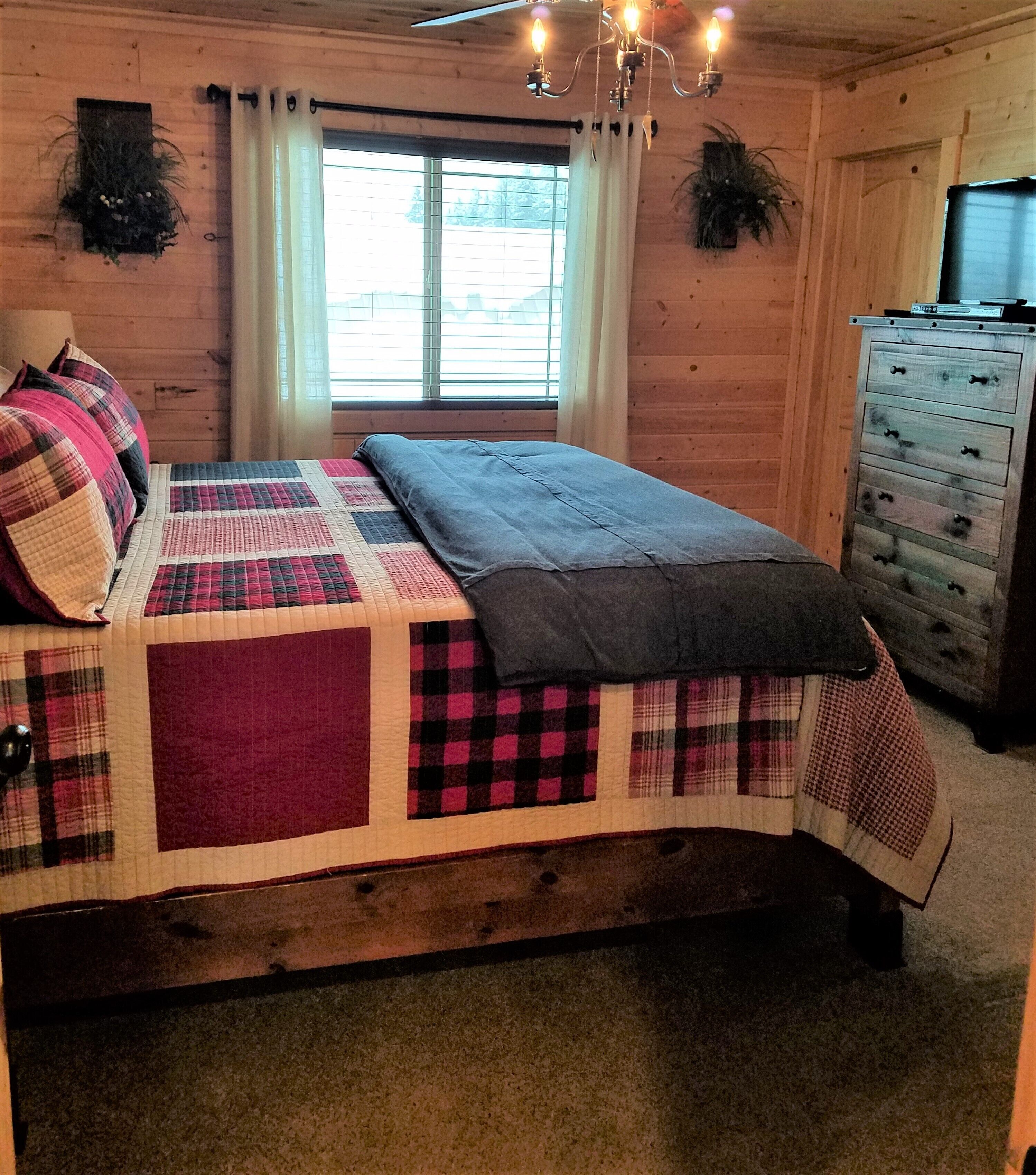 Una habitación de madera con una cama, un tocador y una ventana con cortinas.